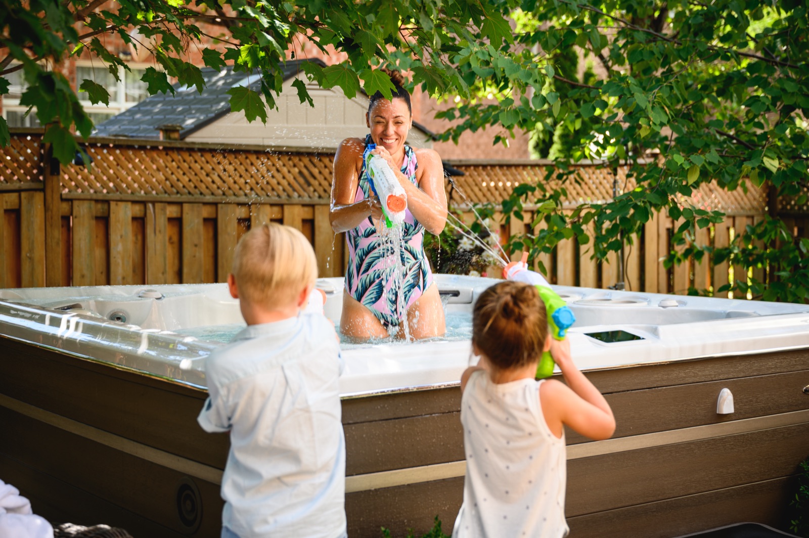 Family enjoying a Hydropool hot tub &mdash; mom and two kids playing with water guns in the backyard
